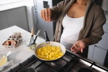 Vista frontal parte média da mulher relaxando em casa, preparando café da manhã na cozinha, polvilhando tempero em ovos mexidos cozinhar em uma panela na placa — Fotografia de Stock