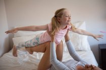 Side view of a Caucasian woman enjoying family time with her daughter at home together, smiling and lifting her daughter above her lying on a bed in their bedroom — Stock Photo