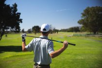 Задній вид на кавказького чоловіка на полі для гольфу в сонячний день з блакитним небом, тримаючи гольф клуб через плечі. — стокове фото