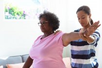Старша змішана жінка проводить час вдома, відвідуючи змішану расу медсестру, медсестра масажує руку — стокове фото