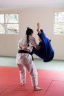 Rear view of two teenage Caucasian and mixed race female judokas wearing blue and white judogi, practicing judo during a sparring in a gym. — Stock Photo