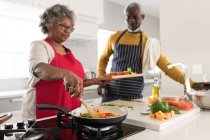 A senior African American couple spending time at home together, social distancing and self isolation in quarantine lockdown during coronavirus covid 19 epidemic, standing in the kitchen preparing food — Stock Photo