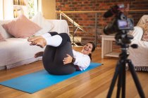 Vlogger mujer caucásica en casa en su sala de estar, demostrando ejercicios para su grabación de blog en línea con una cámara. Distanciamiento social y autoaislamiento en cuarentena. - foto de stock
