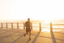 Vista frontale di un maturo uomo caucasico anziano che si allena su una passeggiata in una giornata di sole con cielo blu, correndo al tramonto — Foto stock