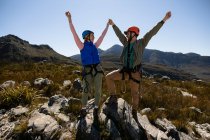 Front view of Caucasian couple enjoying time in nature, wearing zip lining equipment, holding hands with arms in the air, smiling at each other on a sunny day in mountains — Stock Photo