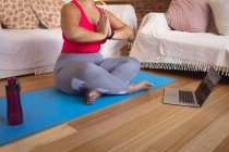 Baixa seção de vlogger feminino em casa em sua sala de estar, praticando ioga e usando seu computador portátil. Distanciamento social e auto-isolamento em quarentena . — Fotografia de Stock