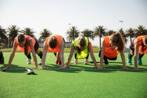 Front view of a group of female Caucasian field hockey players, training before a game, working out on a field hockey pitch, doing push ups, on a sunny day — Stock Photo