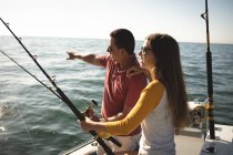 Un hombre caucásico y su hija adolescente sosteniendo cañas de pescar y hablando - foto de stock