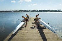 Side view of a rowing team of four Caucasian men preparing rowing boats before rowing, standing on a jetty on the river on a sunny day — Stock Photo