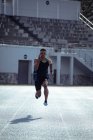 Vista frontale di un atleta maschio di razza mista che pratica in uno stadio sportivo, correndo verso la telecamera. — Foto stock