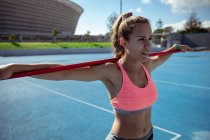 Seitenansicht einer entspannten kaukasischen Athletin, die in einem Sportstadion übt und ihre Arme auf einem über ihren Schultern liegenden Speer ruht — Stockfoto