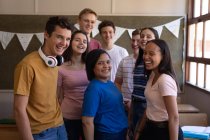 Vista frontale di un gruppo multietnico di alunni adolescenti che si riuniscono in classe e sorridono alla telecamera al momento della pausa — Foto stock