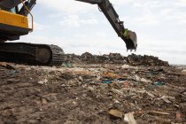 Scavatore di lavoro e di compensazione rifiuti accatastati su una discarica piena di spazzatura con cielo nuvoloso coperto sullo sfondo. Questione ambientale globale dello smaltimento dei rifiuti. — Foto stock
