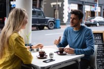 Vista lateral de um casal caucasiano sentado ao lado de uma mesa em um terraço de café, tomando café, conversando e desfrutando de tempo juntos . — Fotografia de Stock