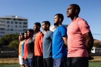 Багато етнічних груп чоловіків п'ять гравців на боці футболістів у спортивному одязі, які тренуються на спортивному полі на сонці, стоячи в ряд перед грою . — стокове фото