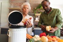 Glückliche ältere afroamerikanische Rentnerehepaar zu Hause, Essen zubereiten, Gemüse schneiden, die Gemüseabfälle in einen Kompostbehälter in ihrer Küche, zu Hause zusammen isolieren während Coronavirus covid19 Pandemie — Stockfoto