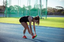 Side view of a Caucasian female athlete practicing at a sports stadium, stretching, bending down on a running track to touch her toes — Stock Photo