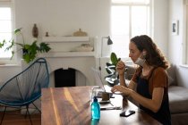 Белая женщина проводит время дома в маске против коронавируса, ковид 19, сидит за столом и работает, используя ноутбук и наушники. Социальное дистанцирование и самоизоляция в карантинной изоляции. — стоковое фото