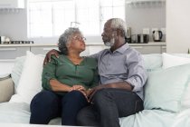 Una coppia afroamericana anziana che trascorre del tempo a casa insieme, distanziamento sociale e isolamento in quarantena durante l'epidemia di coronavirus covid 19, seduta su un divano, abbracciando e parlando — Foto stock