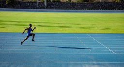Vista laterale di un atleta maschio di razza mista che pratica in uno stadio sportivo, sprint. — Foto stock