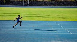 Vista lateral de un atleta masculino de raza mixta practicando en un estadio deportivo, corriendo. - foto de stock