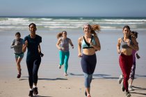Вид спереди на многоэтническую группу подруг, наслаждающихся упражнениями на пляже в солнечный день, бегущих по берегу моря. — стоковое фото