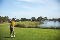 Вид сзади на кавказца на поле для гольфа в солнечный день с голубым небом, ударяющего мячом для гольфа — стоковое фото