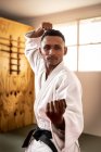 Front view close up of a focused teenage mixed-race male judoka wearing white judogi, warming up before a training in a gym, striking a pose, punching the air. — Stock Photo