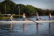 Side view of a rowing team of four Caucasian women training on the river, rowing in a racing shell — Stock Photo