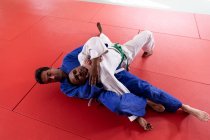 Vue en angle élevé avant d'un entraîneur de judo masculin mixte et d'un judoka masculin mixte adolescent portant du judoka bleu et blanc, pratiquant le judo lors d'un entraînement dans une salle de gym. — Photo de stock