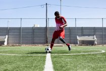 Jogador de futebol masculino de raça mista com perna protética vestindo um treinamento de tira de equipe em um campo de esportes ao sol, aquecendo a bola de chute. — Fotografia de Stock