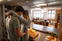 Seitenansicht eines jungen Mannes mit gemischter Rasse und einer jungen kaukasischen Frau, die in der Küche stehen und sich beim gemeinsamen Frühstück umarmen. — Stockfoto