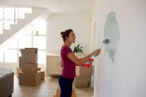 Caucasian woman spending time at home self isolating and social distancing in quarantine lockdown during coronavirus covid 19 epidemic, painting the walls of her home. — Stock Photo