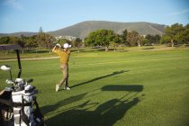Вид сбоку на кавказца на поле для гольфа в солнечный день с голубым небом, ударяющего мячом для гольфа — стоковое фото
