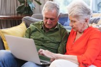 Close up of a retired senior Caucasian couple at home sitting on a sofa in their living room, talking and using a laptop computer together, couple isolating during coronavirus covid19 pandemic — Stock Photo