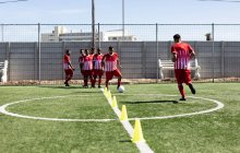 Multi ethnic team of male five a side football players wearing a team strip training at a sports field in the sun, warming up tackling with ball between cones. — Stock Photo