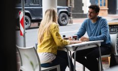 Vista lateral de um casal caucasiano sentado ao lado de uma mesa em um terraço de café, tomando café, conversando e desfrutando de tempo juntos . — Fotografia de Stock