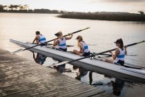 Side view of a female rowing team of four young adult Caucasian women sitting in a racing shell on the river and pushing it away from the jetty before rowing training — Stock Photo