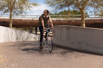 Vista frontale di un uomo di razza mista con lunghi dreadlocks in giro per la città in una giornata di sole, in bicicletta per strada. — Foto stock