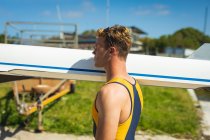 Side view close up of a Caucasian male rower carrying a boat on his shoulders, walking along a jetty on the river, on a sunny day — Stock Photo