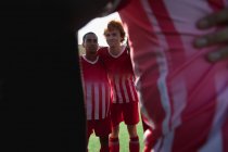 Vista frontal de uma raça mista e um adolescente caucasiano jogador de hóquei em campo se preparando antes de um jogo, em um huddle com grupo multi-étnico de jogadores do sexo masculino em sua equipe, interagindo em um dia ensolarado no campo antes de um jogo — Fotografia de Stock