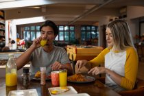 Frontansicht eines jungen Mannes mit gemischter Rasse und einer jungen kaukasischen Frau, die an einem Tisch sitzen und gemeinsam frühstücken. — Stockfoto