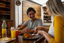 Front view of a young mixed race man and a young Caucasian woman sitting by a table and enjoying breakfast together. — Stock Photo