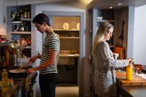 Vue latérale d'un jeune homme métis et d'une jeune femme caucasienne debout dans la cuisine et préparant le petit déjeuner ensemble. — Photo de stock