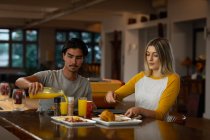 Vista frontale di un giovane uomo di razza mista e una giovane donna caucasica seduti accanto a un tavolo e che fanno colazione insieme. — Foto stock