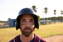 Ritratto di un giocatore di baseball caucasico, con indosso un'uniforme e un casco, in piedi su un campo da baseball, che guarda una telecamera — Foto stock