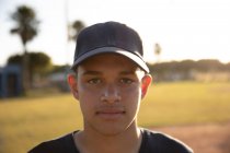 Портрет бейсболиста смешанной расы, одетого в командную форму и кепку, стоящего на бейсбольном поле, смотрящего в камеру — стоковое фото
