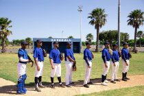 Vista lateral de un grupo multiétnico de jugadores de béisbol masculinos, preparándose antes de un partido, de pie en fila, preparándose para cantar un himno nacional - foto de stock