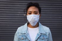 Porträt einer Mischlingshündin mit langen dunklen Haaren, die tagsüber auf den Straßen der Stadt unterwegs ist, eine Gesichtsmaske gegen Luftverschmutzung und Coronavirus trägt, stehend in die Kamera blickt, im Hintergrund eine graue Wand. — Stockfoto