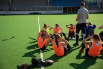 Side view of a group of female Caucasian field hockey players and their Caucasian field hockey coach, training before a game, working out on a field hockey pitch, exercising, doing sit ups, on a sunny day — Stock Photo
